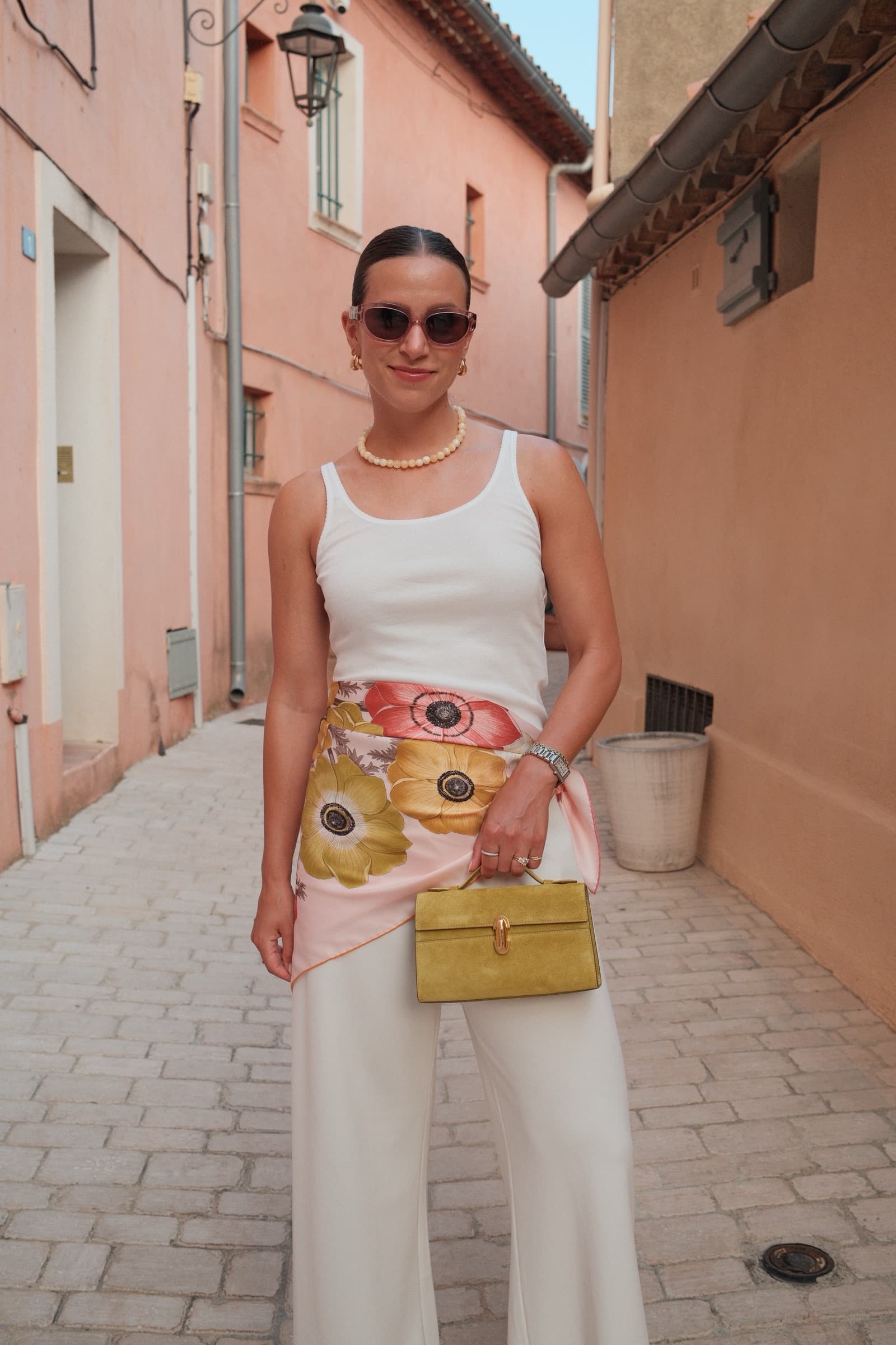 Erika Schatz in a white outfit with a floral scarf in a Mediterranean alley.